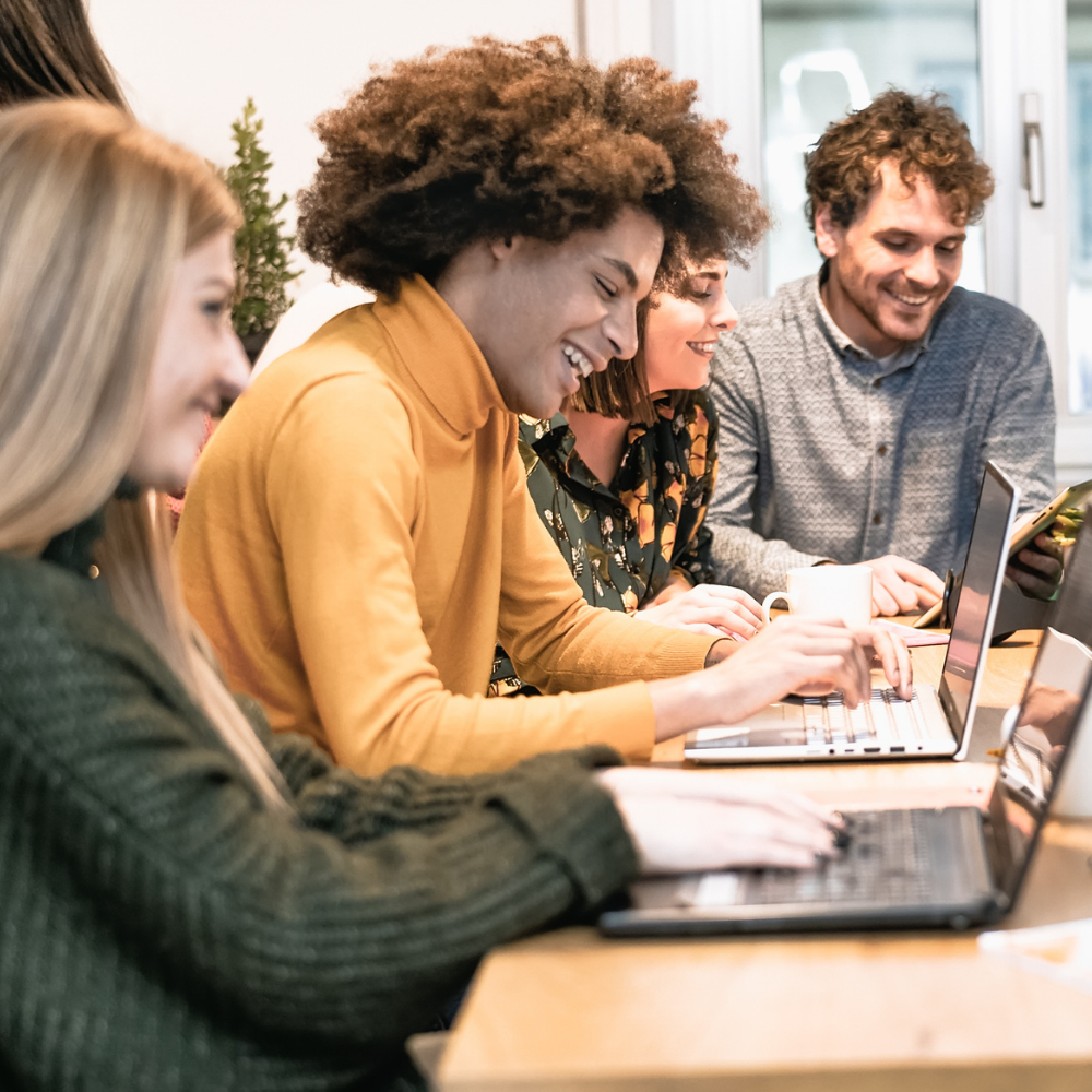 People sitting around a desk with their laptops. 